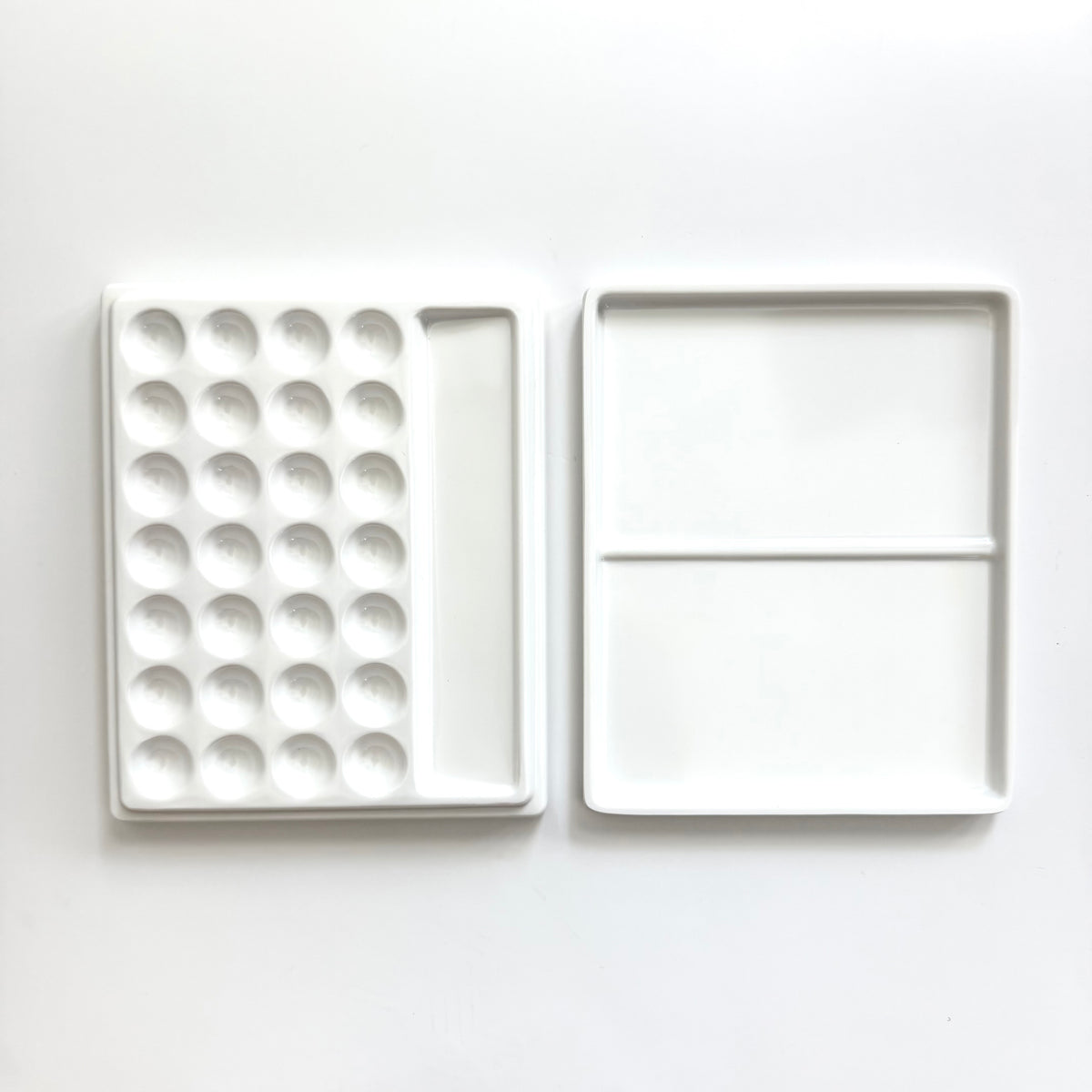 A white ceramic paint palette shown open, displaying a left side with multiple circular wells and a right side with two larger square pans divided by a horizontal line, set against a plain white background.