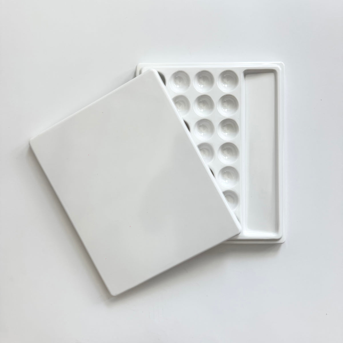 A white ceramic paint palette with a matching lid, shown open to reveal multiple round wells and a narrow rectangular well, photographed on a clean white background.