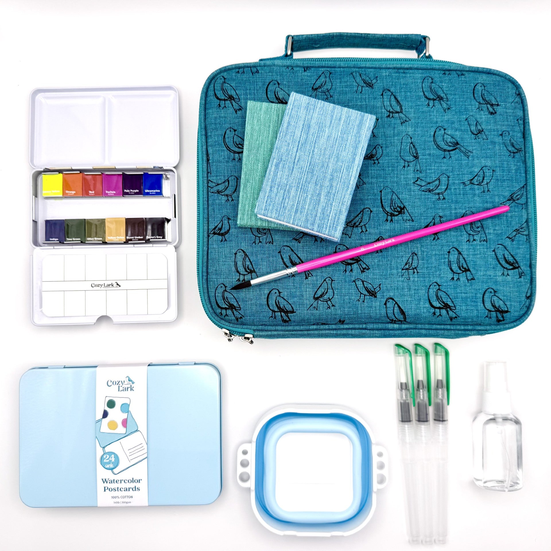 Art supply set with watercolor paints, brushes, postcards, accordion books and travel case on a white background