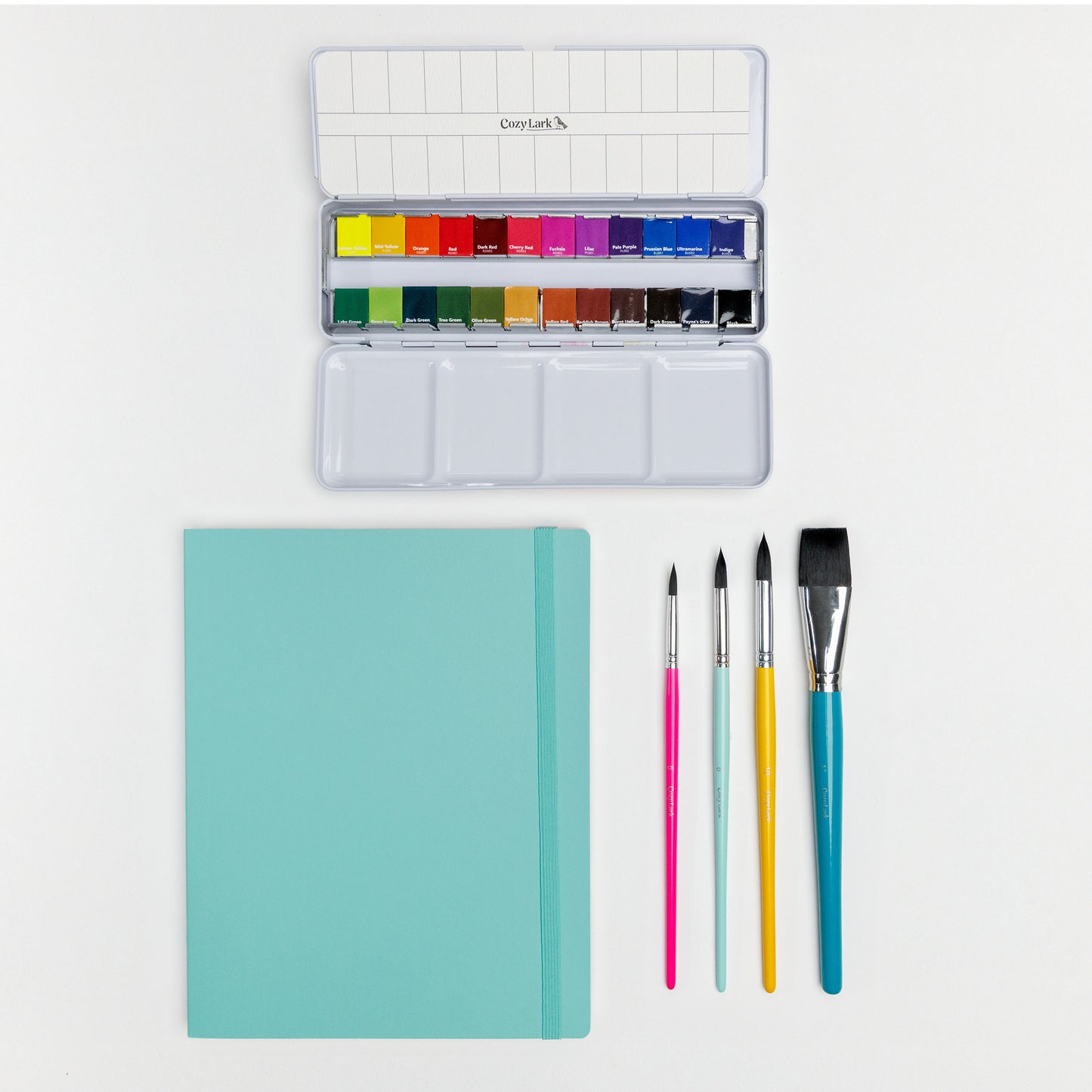 Flat lay of Cozy Lark watercolor palette, artist tape, pigment liners, brushes, and teal practice book on white background