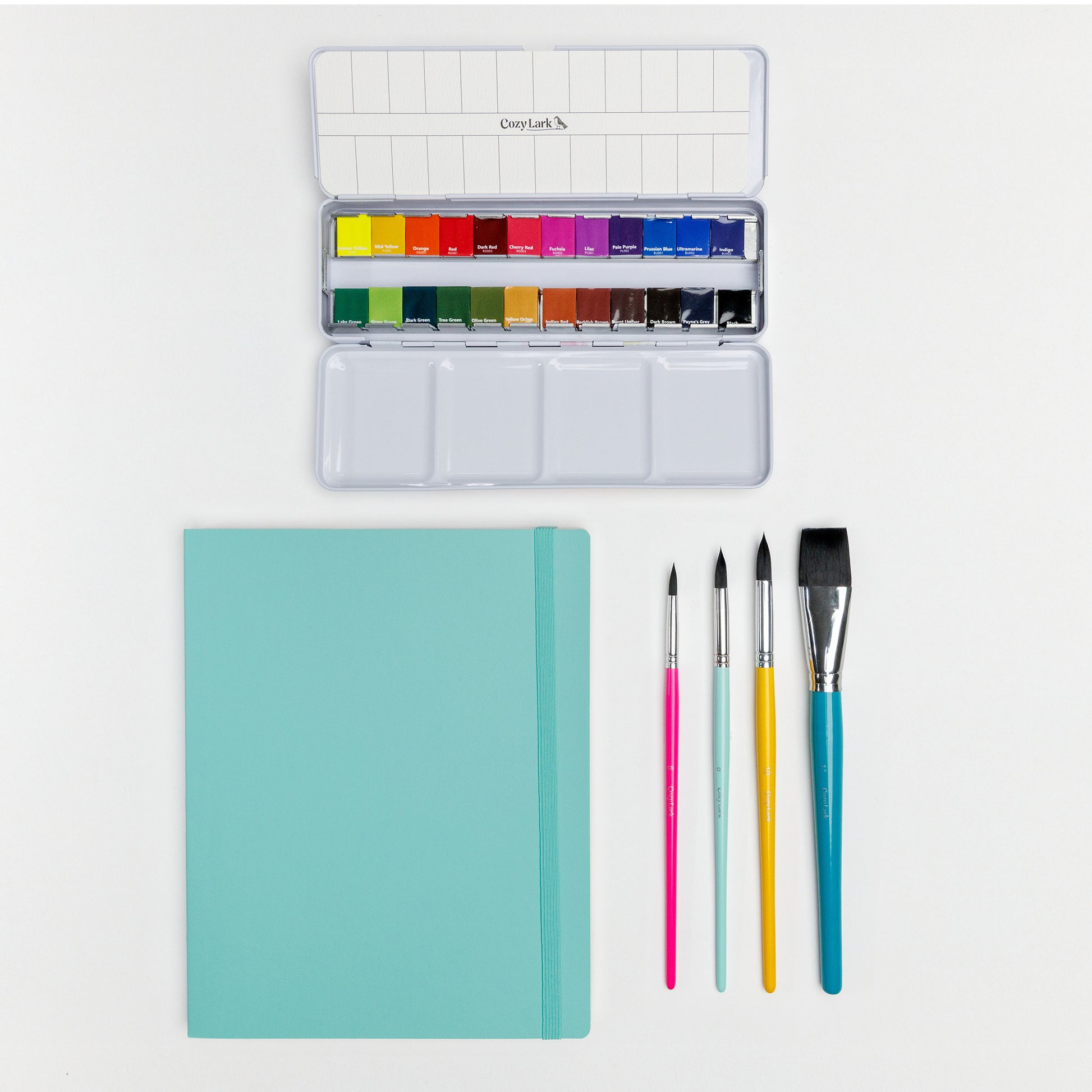 Flat lay of Cozy Lark watercolor palette, artist tape, pigment liners, brushes, and teal practice book on white background