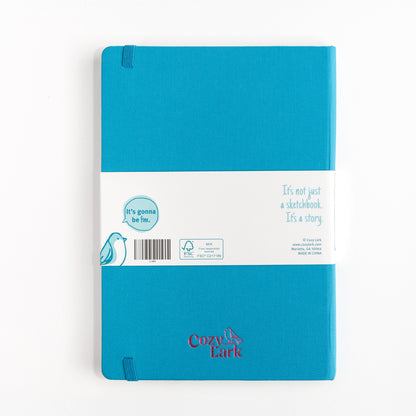 Blue hardcover essential sketchbook with Cozy Lark imprint in pink centered at the bottom on a white background
