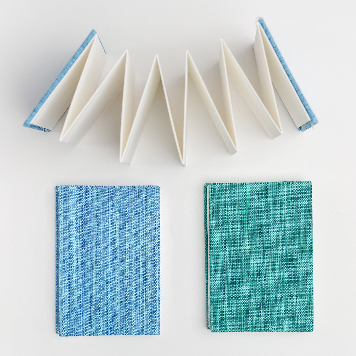 Set of bookcloth covered mini accordion sketchbooks, one blue and one teal, with open accordion book viewed from above