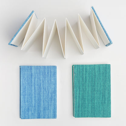Set of bookcloth covered mini accordion sketchbooks, one blue and one teal, with open accordion book viewed from above