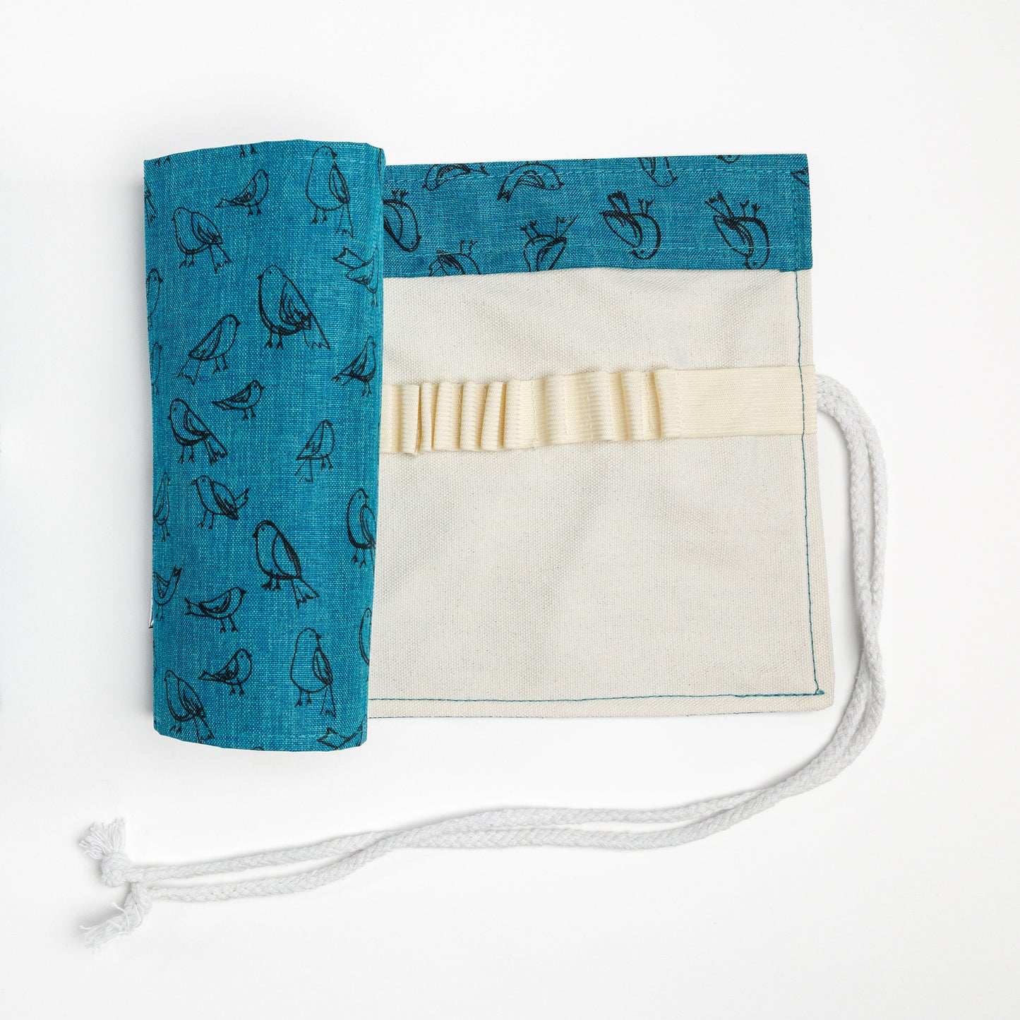 Partially open pencil roll with dark teal fabric printed with illustrated birds on the outside and natural canvas on the inside. Elastic loops and folded section at top to protect pencil points