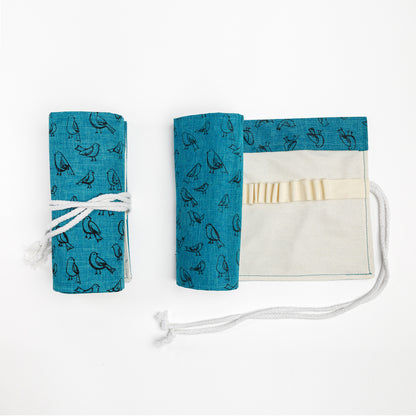 One rolled and one partially open pencil roll with dark teal fabric printed with illustrated birds on the outside, and natural canvas on the inside. 