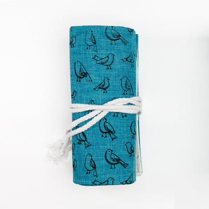 Rolled up pencil roll with dark teal fabric printed with a illustrated bird pattern and light tie cord.
