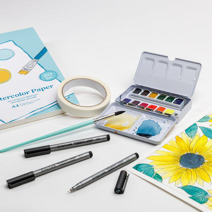 Cozy Lark watercolor starter setup with paper pad, artist  tape, open 12-color palette, Size 8 Round brush, pigment liners, and sunflower painting in progress