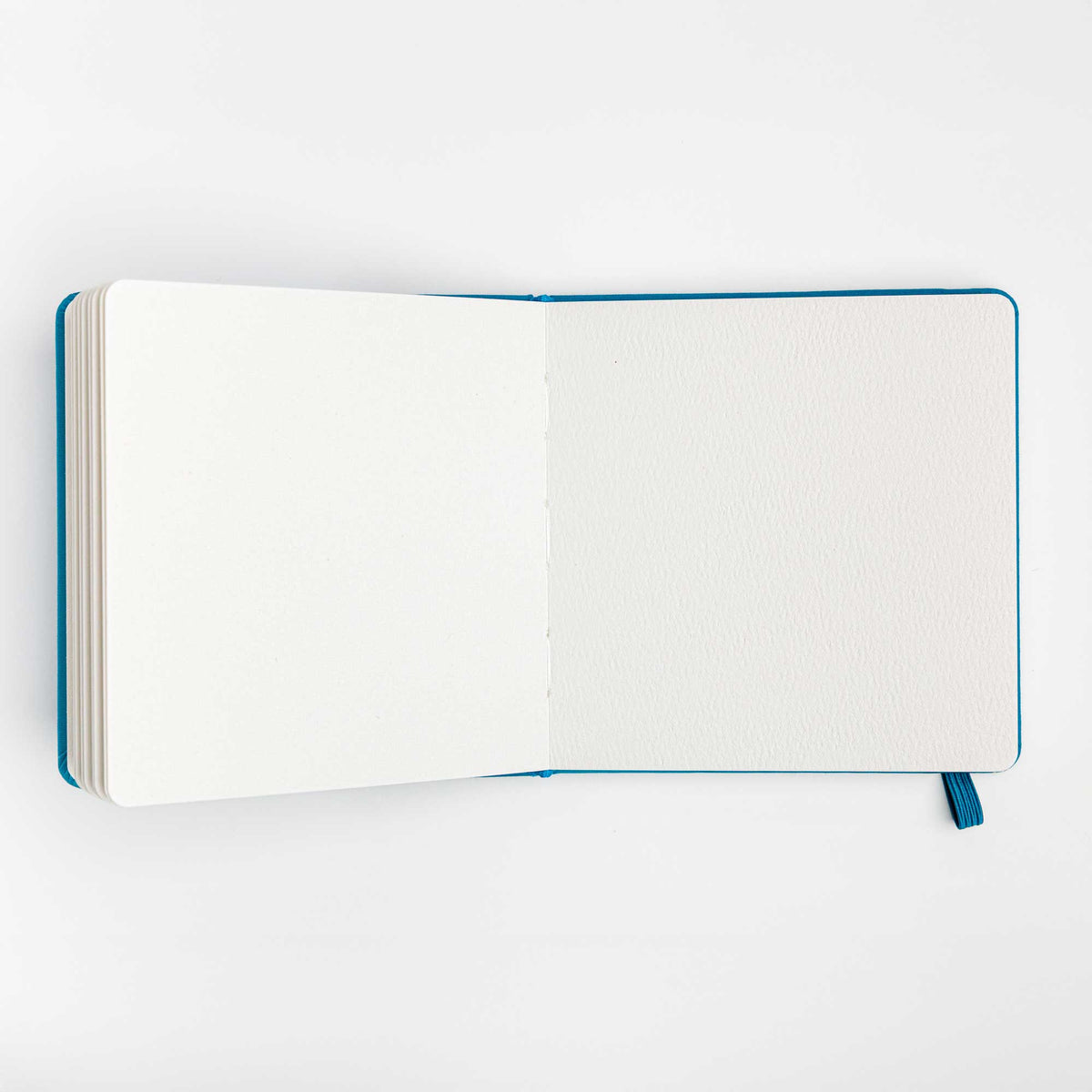 Open view of the travel notebook showing blank watercolor paper pages on a white background.
