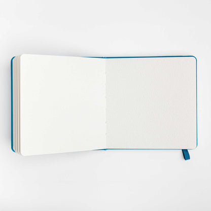 Open view of the travel notebook showing blank watercolor paper pages on a white background.